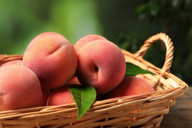 Photo of Fresh peaches and leaves in basket on table against blurred green background, closeup