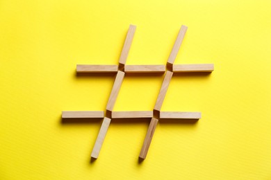 Hashtag symbol made of wooden blocks on yellow background, top view