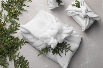 Furoshiki technique. Gifts packed in white fabric and thuja branches on grey marble table, flat lay