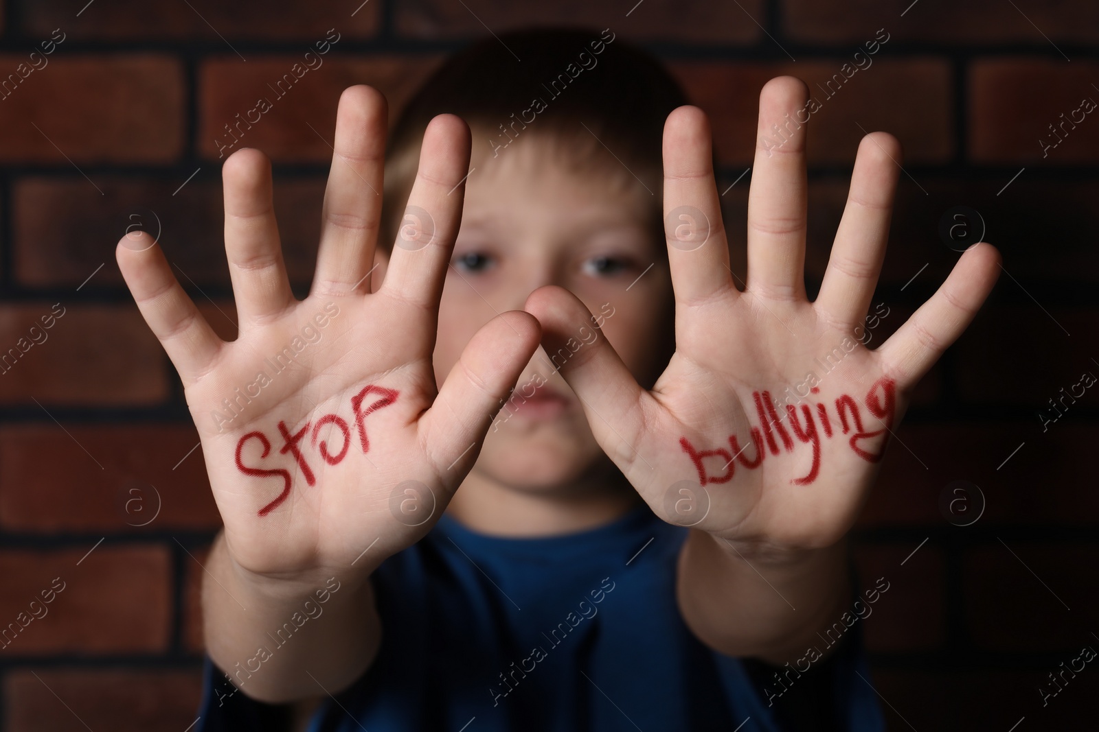Photo of Kid showing hands with phrase Stop Bullying near brick wall, selective focus