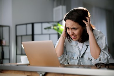 Emotional woman working on laptop in office. Online hate concept