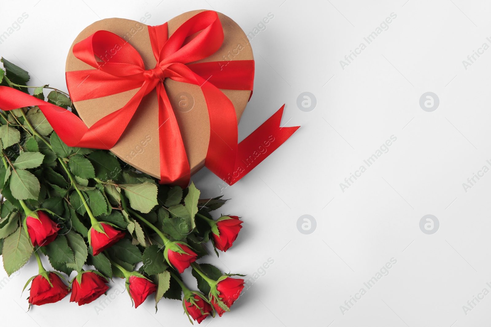 Photo of Heart shaped gift box with bow and beautiful red roses on white background, flat lay. Space for text