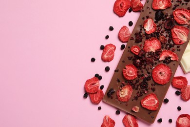 Photo of Chocolate bar with freeze dried fruits on pink background, flat lay. Space for text