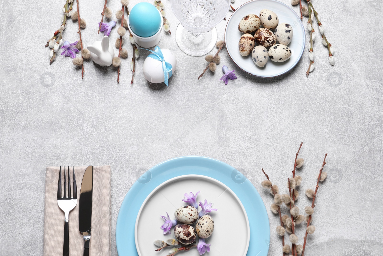 Photo of Festive Easter table setting with painted eggs and floral decor on light grey background, flat lay. Space for text