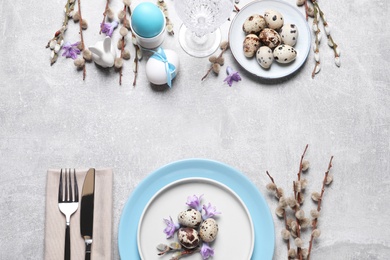 Festive Easter table setting with painted eggs and floral decor on light grey background, flat lay. Space for text