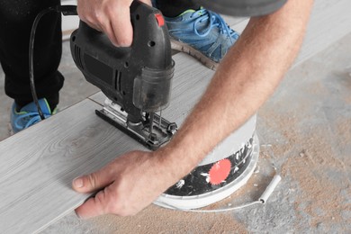 Photo of Professional worker using jigsaw during installation of new laminate flooring, closeup