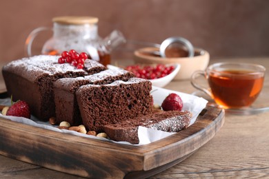 Photo of Tasty chocolate sponge cake with nuts and berries on wooden table, closeup