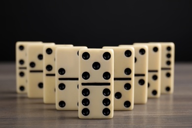 Photo of Domino tiles on wooden table against black background, closeup