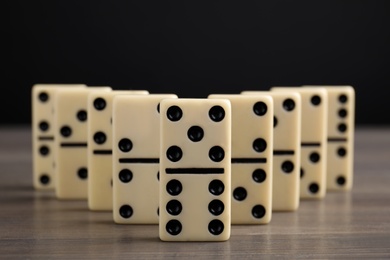 Domino tiles on wooden table against black background, closeup