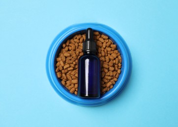 Photo of Glass bottle of tincture and dry pet food in bowl on light blue background, top view
