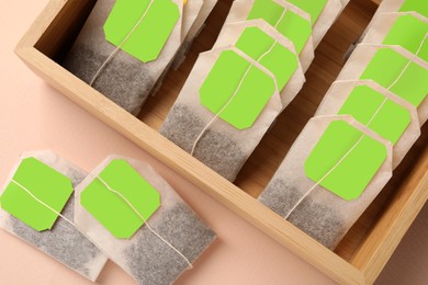 Many tea bags in wooden box on color background, flat lay