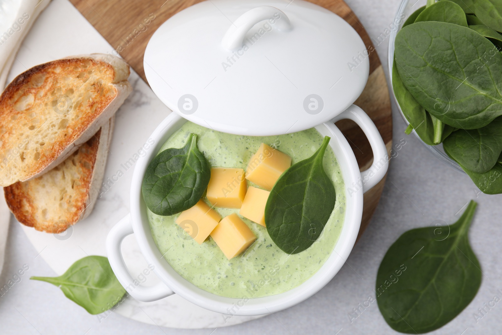 Photo of Delicious spinach cream soup with cheese in bowl on light grey table, flat lay