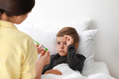 Mother measuring temperature of her sick son in bed