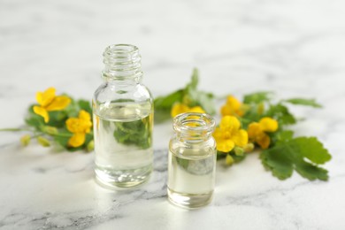 Bottles of natural celandine oil near flowers on white marble table