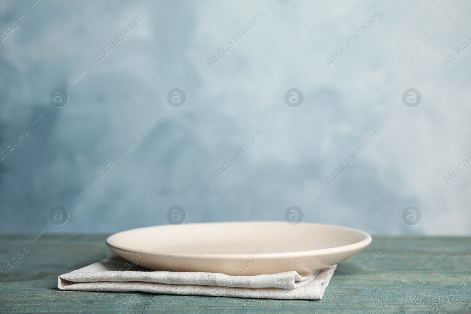 Photo of Empty plate and towel on light blue wooden table. Space for text