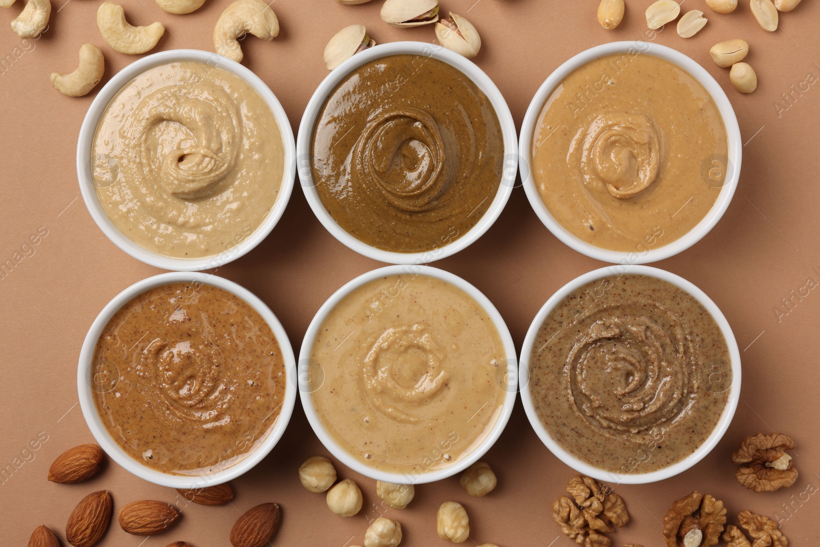 Photo of Many tasty nut butters in bowls and nuts on beige table, flat lay