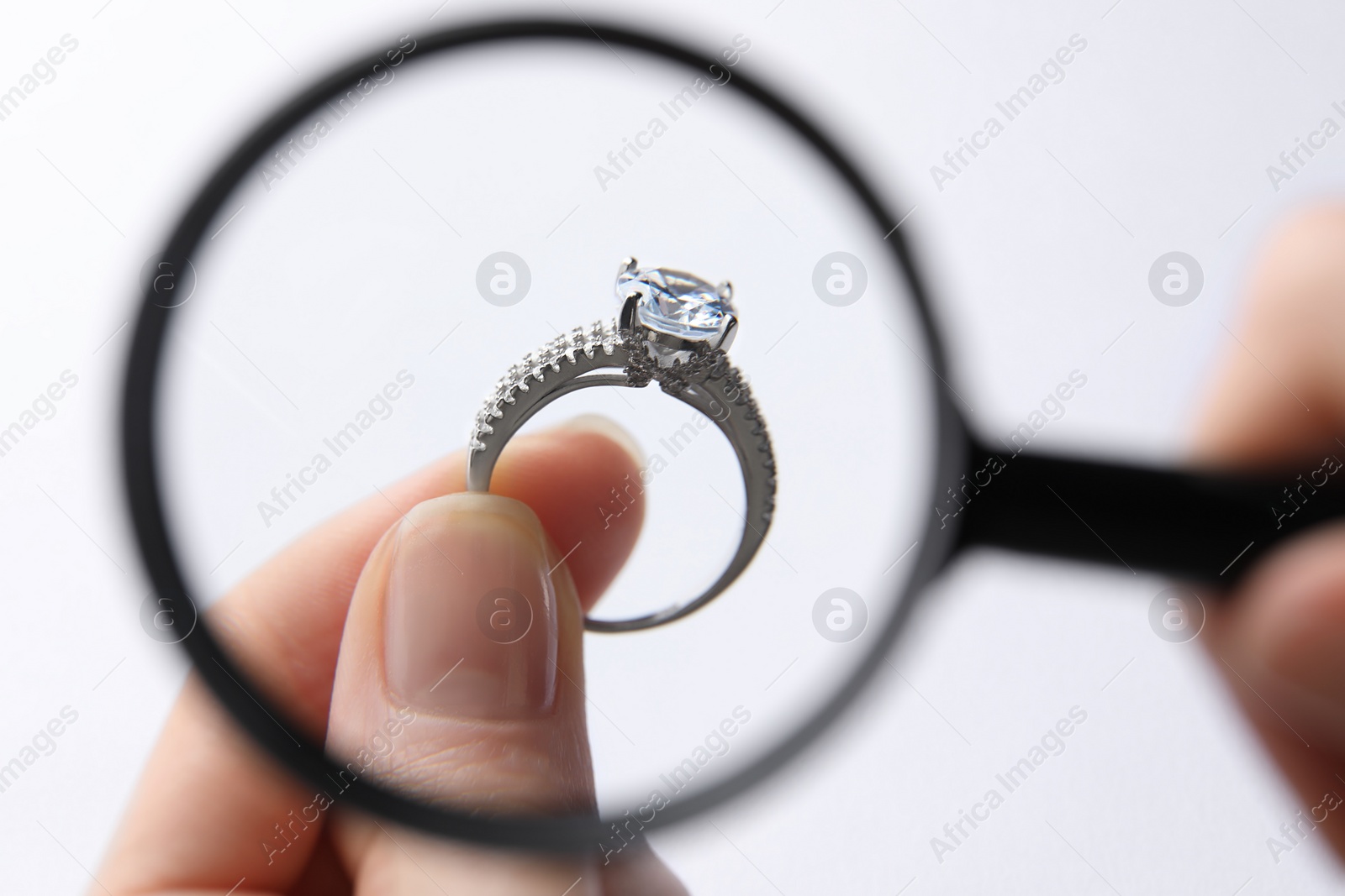 Photo of Jeweler examining diamond ring with magnifying glass on white background, closeup