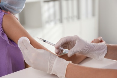 Doctor vaccinating little girl in hospital, closeup. Health care