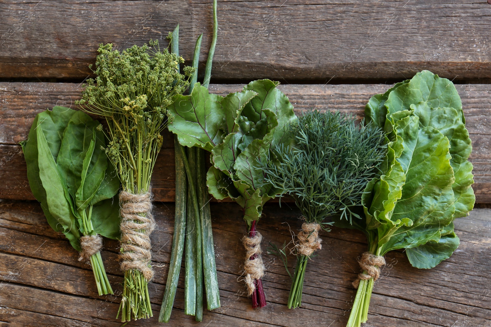 Photo of Bunches of different herbs on wooden table, flat lay