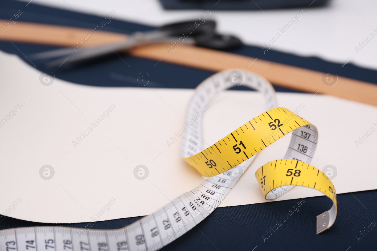 Photo of Measuring tape, paper template and fabric on table in tailor workshop, closeup