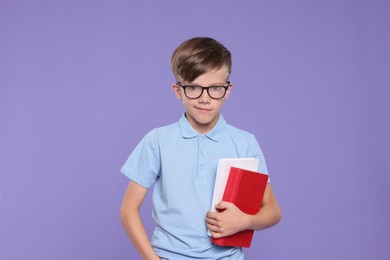 Cute schoolboy in glasses holding books on violet background