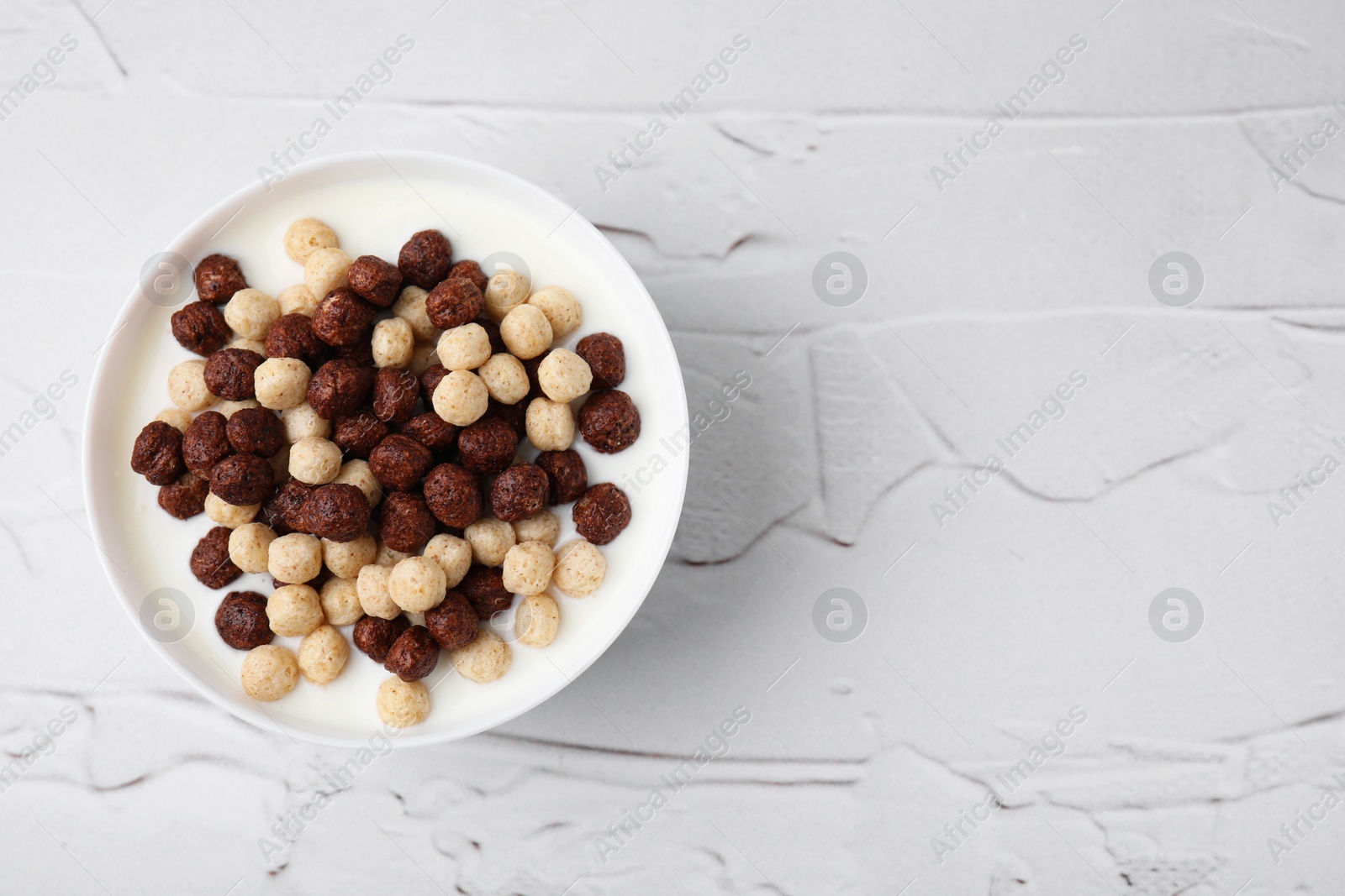 Photo of Breakfast cereal. Tasty corn balls with milk in bowl on white textured table, top view. Space for text