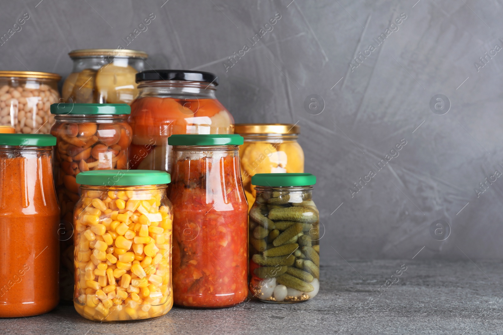 Photo of Jars of tasty pickled vegetables on grey table. Space for text