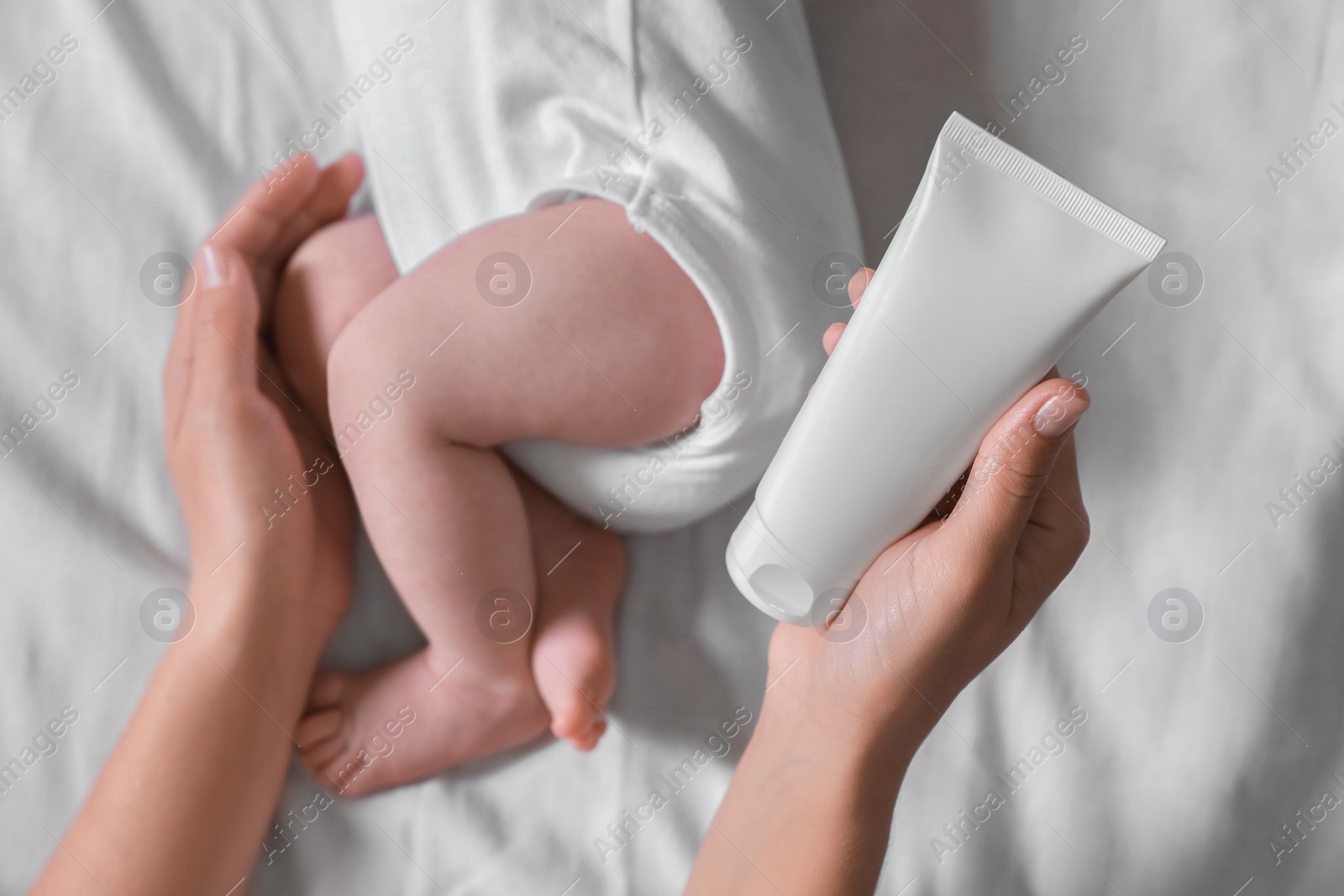 Photo of Mother with cream near little baby on bed, top view