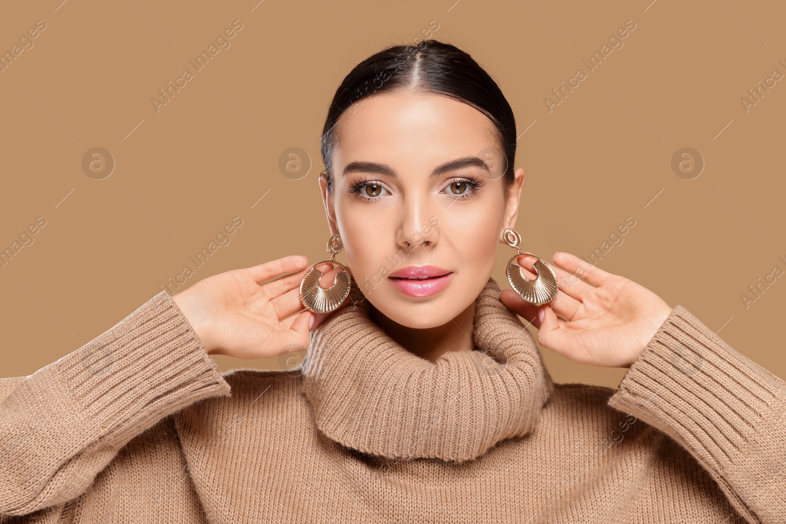 Photo of Beautiful young woman with elegant earrings on light brown background