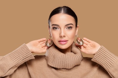 Beautiful young woman with elegant earrings on light brown background