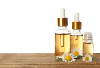 Chamomile flowers and cosmetic bottles of essential oil on wooden table against white background. Space for text