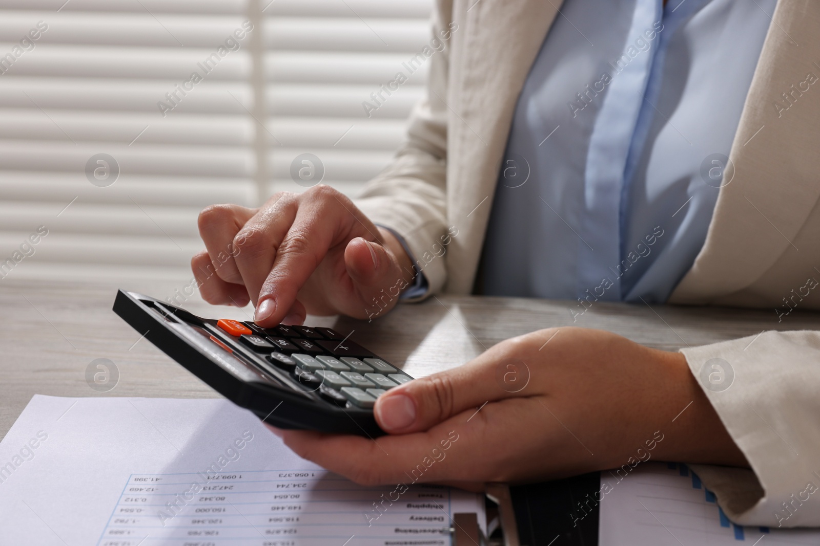 Photo of Woman using calculator at table in office, closeup