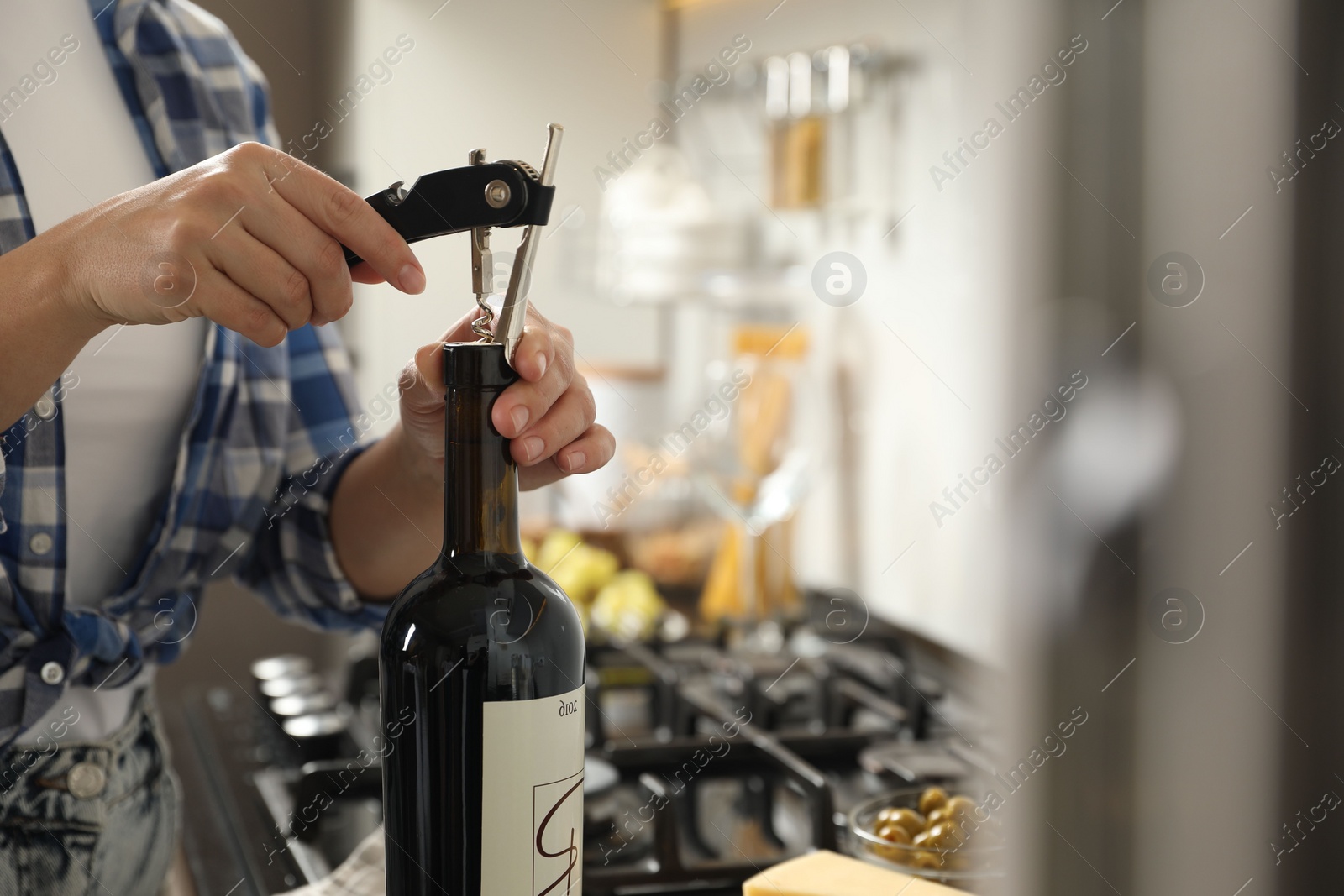 Photo of Woman opening wine bottle with corkscrew indoors, closeup. Space for text