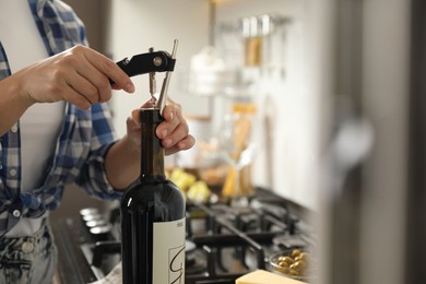 Woman opening wine bottle with corkscrew indoors, closeup. Space for text