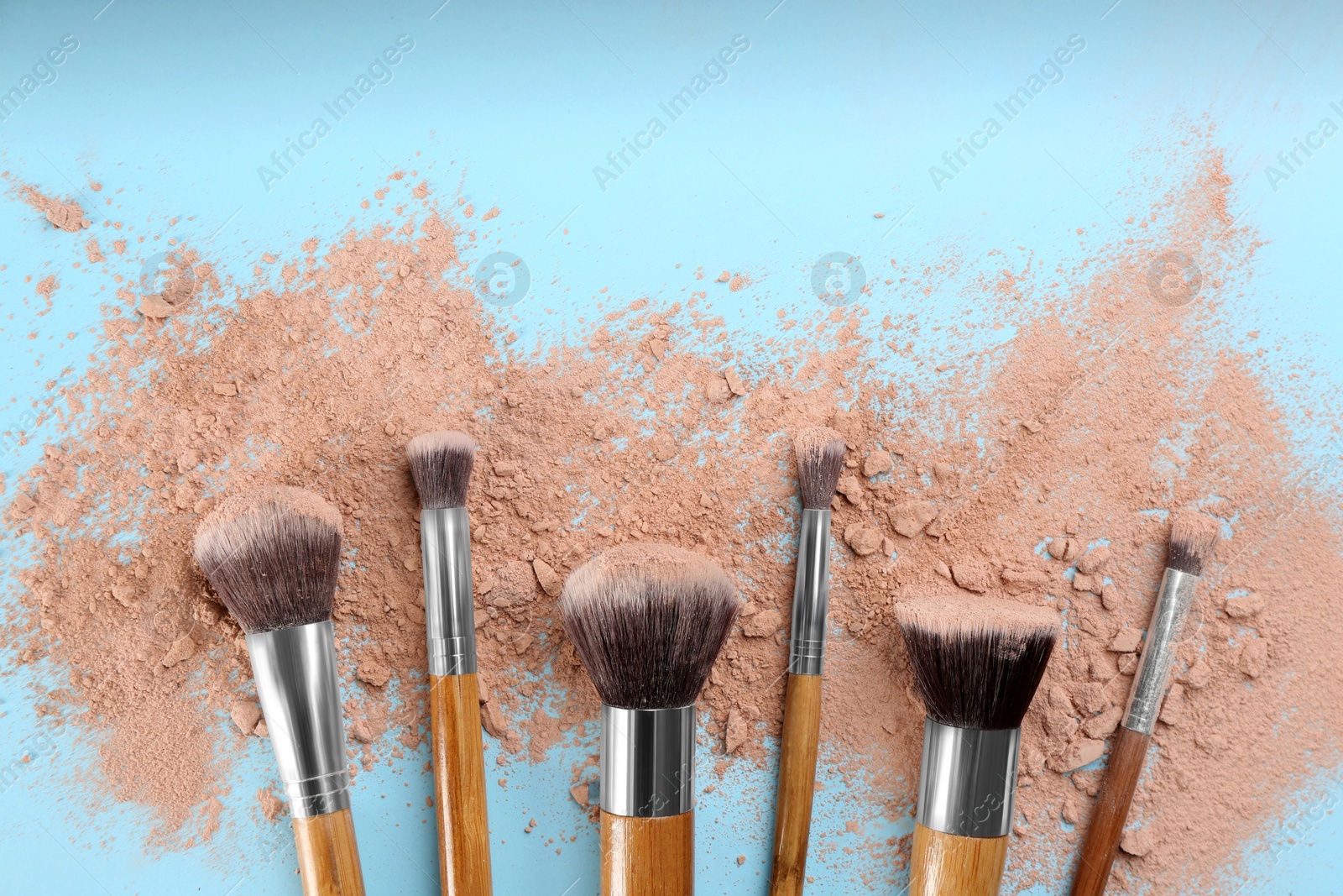 Photo of Brushes and scattered face powder on light blue background, flat lay