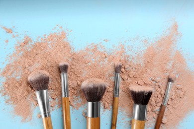 Brushes and scattered face powder on light blue background, flat lay