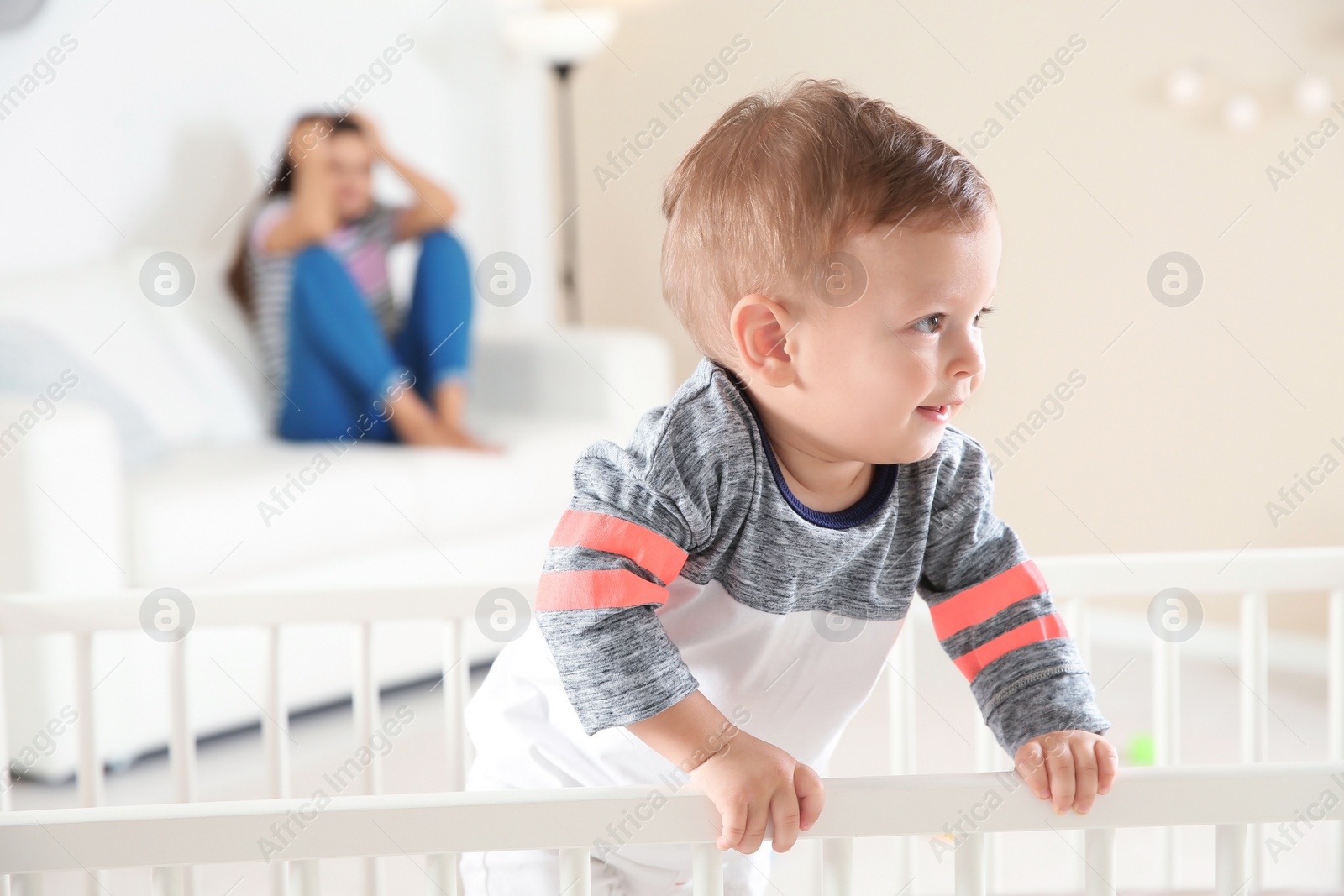 Photo of Cute baby boy in crib and young mother suffering from postnatal depression on blurred background