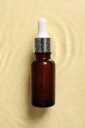 Bottle of cosmetic serum and water on beige background, top view