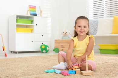 Cute little girl playing with toy on floor at home, space for text