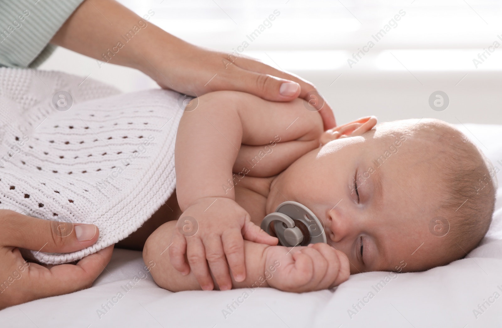 Photo of Mother covering her sleeping baby with knitted blanket at home