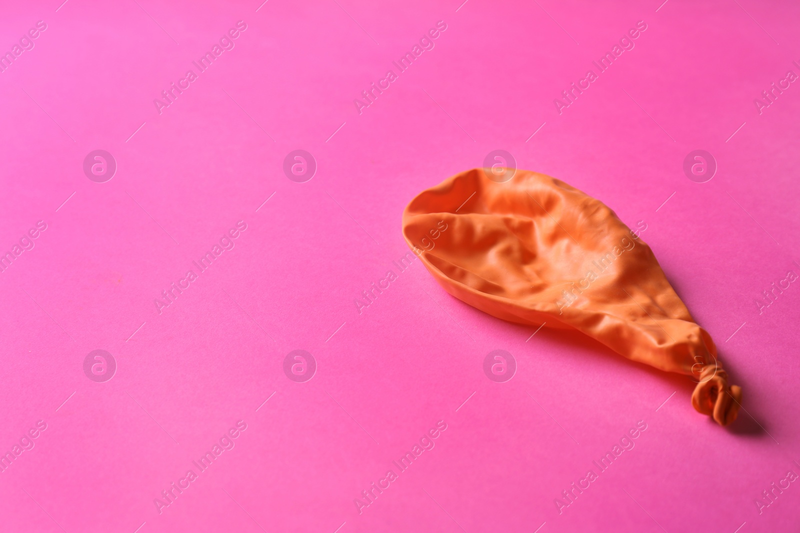 Photo of Orange deflated balloon on color background, space for text