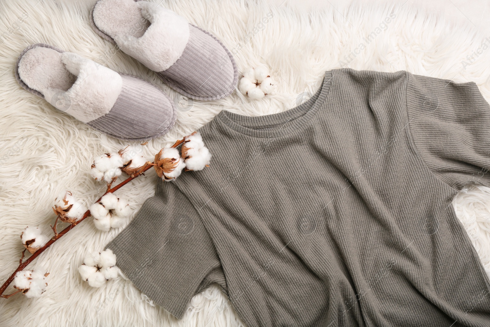 Photo of Pair of slippers, pajamas and cotton flowers on fuzzy carpet, flat lay. Comfortable home outfit