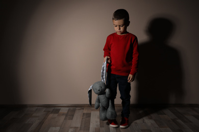 Photo of Sad little boy with toy near beige wall, space for text. Domestic violence concept