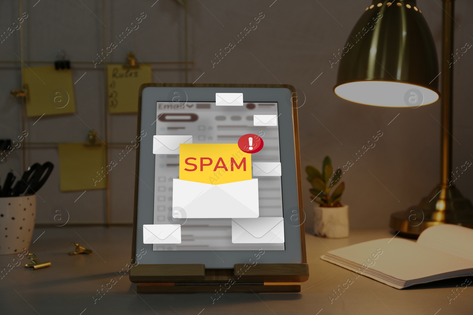 Image of Spam warning message in email software. Envelope illustrations popping out of tablet display on office desk