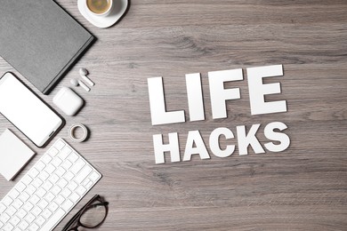 Words Life Hacks, computer keyboard, smartphone and stationery on wooden table, flat lay. Workplace with cup of coffee