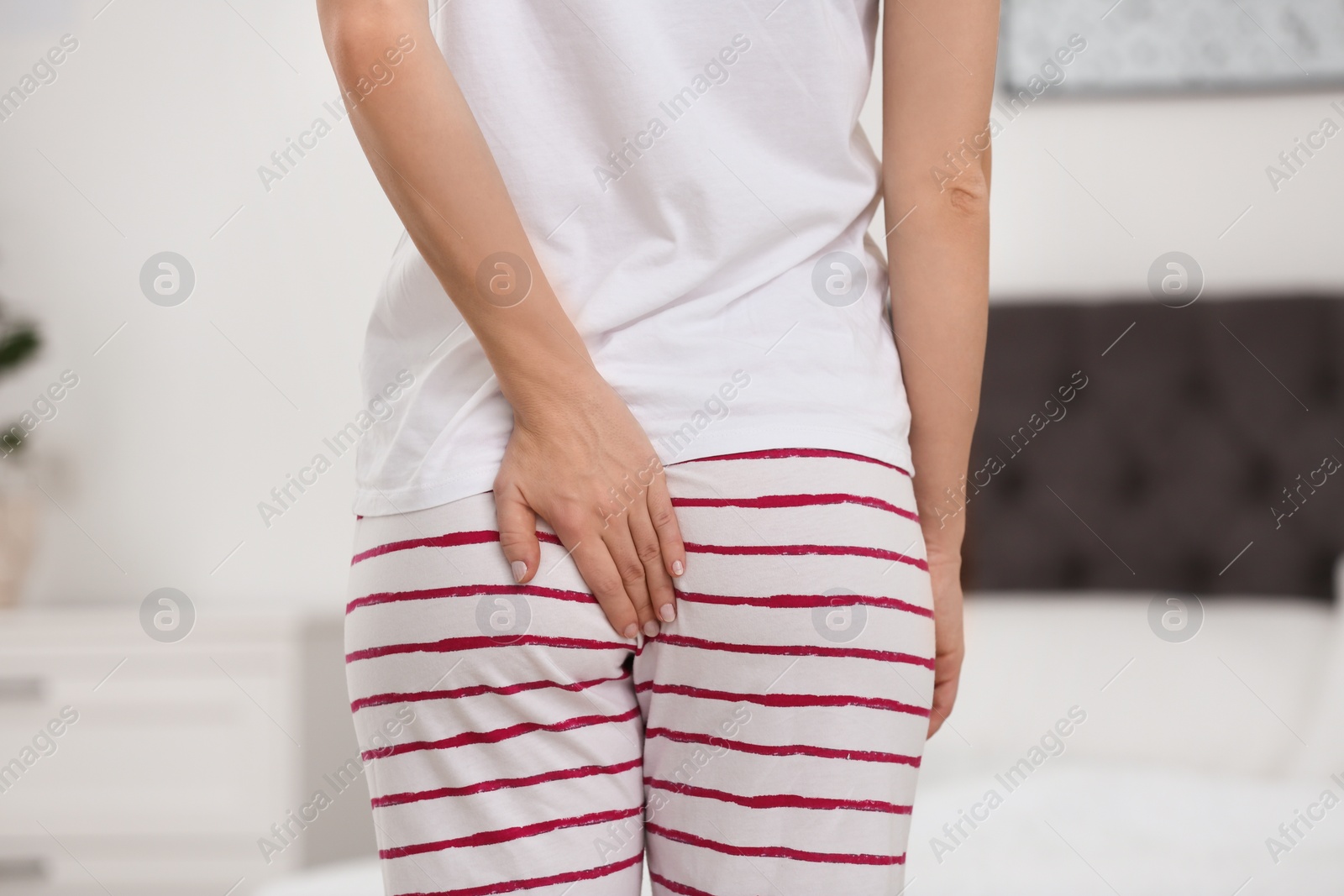 Photo of Young woman suffering from hemorrhoid in bedroom, closeup