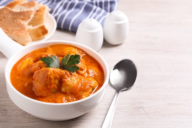 Photo of Bowl of delicious chicken curry on white wooden table, space for text