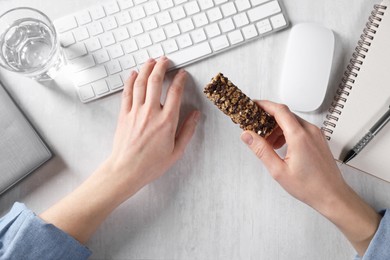 Photo of Woman holding tasty granola bar working with computer at light table, top view