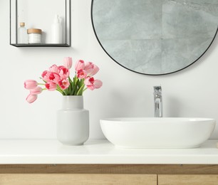 Photo of Vase with beautiful pink tulips and toiletries near sink in bathroom