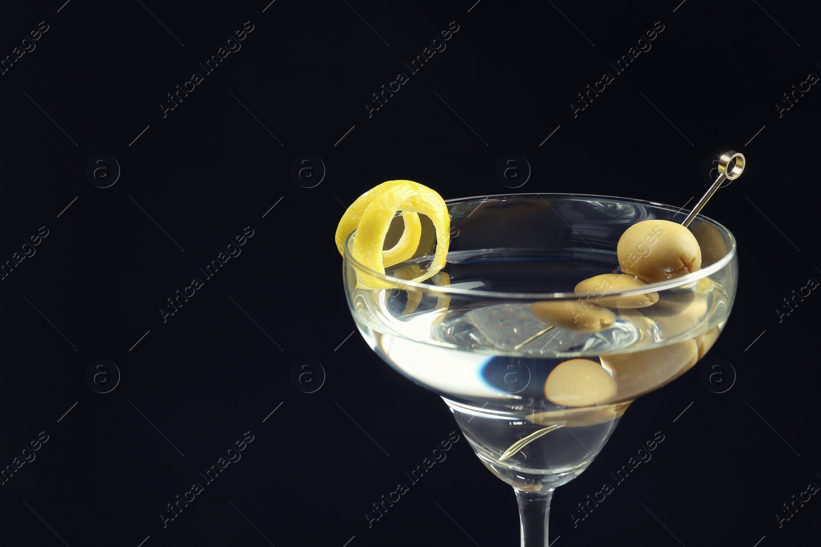 Photo of Martini cocktail with olives and lemon twist on dark background, closeup. Space for text